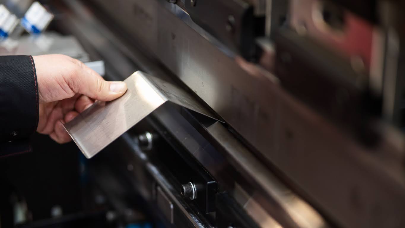Hand holding a sheet of metal against a press brake machine.